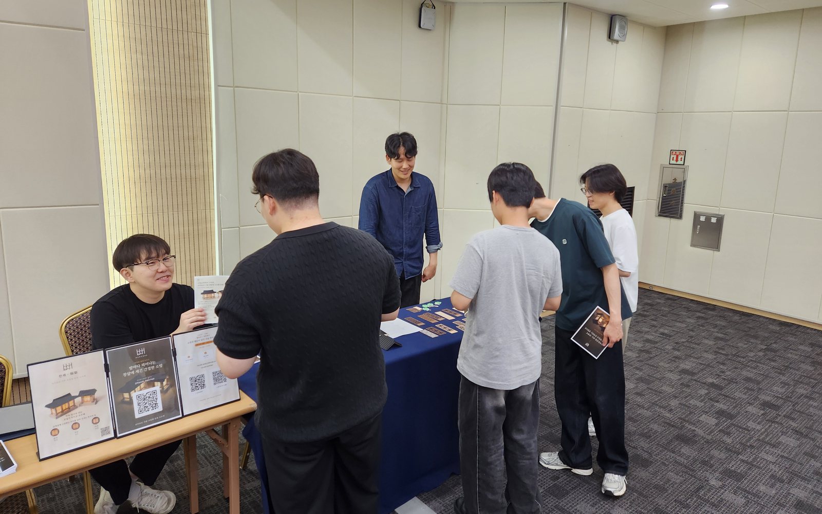 전북대학교 졸업전시 한채 부스에서 팀원이 안내판 옆에서 관람객에게 볕채와 문창살 책갈피를 설명하는 모습