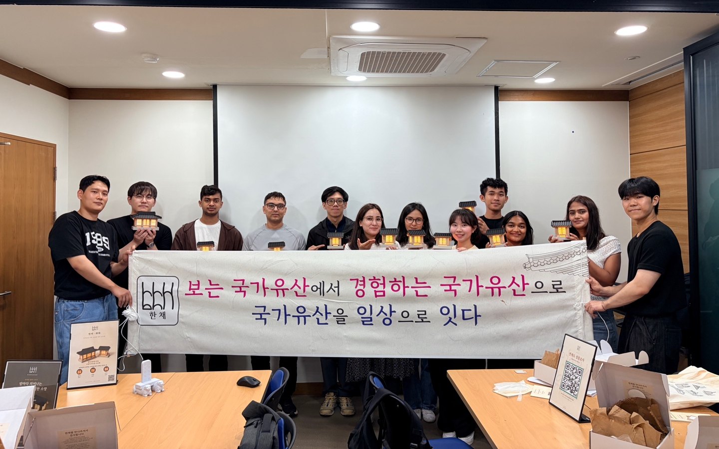 볕채 한칸 조명과 ‘보는 국가유산에서 경험하는 국가유산으로’ 현수막을 함께 든 전북대 유학생과 한채 팀 단체사진